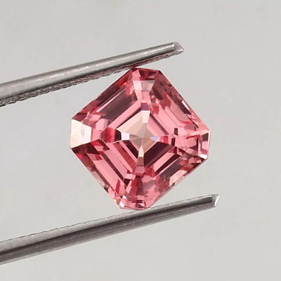 Natural Padparadscha Sapphire gemstone held by tweezers on a gray background