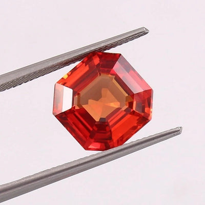 Red octagonal orange sapphire held between tweezers on a light pink background