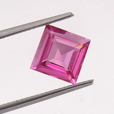 Square-cut pink Sapphire gemstone held between tweezers on a white background