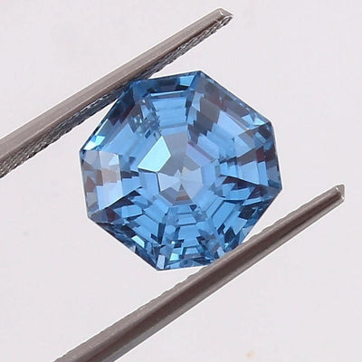 Swiss Blue Topaz gemstone held between tweezers on a light gray background