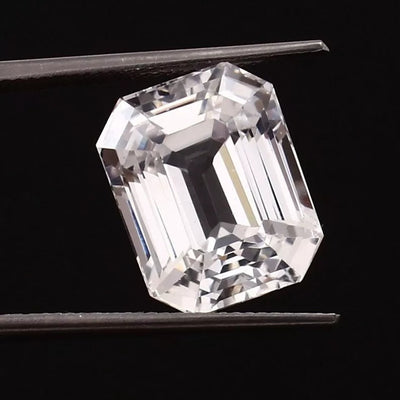 emerald cut White Sapphire held by tweezers against a black background