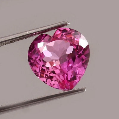 Heart-shaped pink sapphire held by tweezers on a gray background