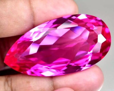 mogok pink ruby pear held between fingers against a neutral background