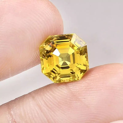 Yellow Sapphire gemstone held between fingers against a neutral background