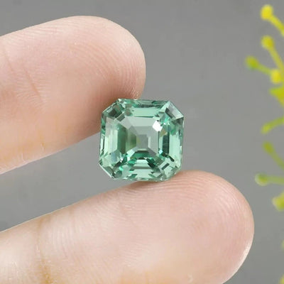Green Sapphire gemstone held between fingers against a neutral background