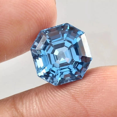Blue Brazilian Aquamarine gemstone held between fingers against a neutral background