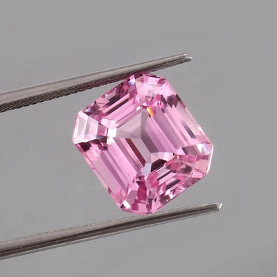 Pink Morganite Madagascar gemstone held between tweezers against a gray background
