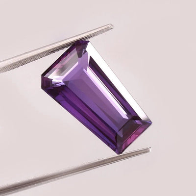 Purple Pink Taaffeite Sapphire gemstone held between tweezers on a light gray background
