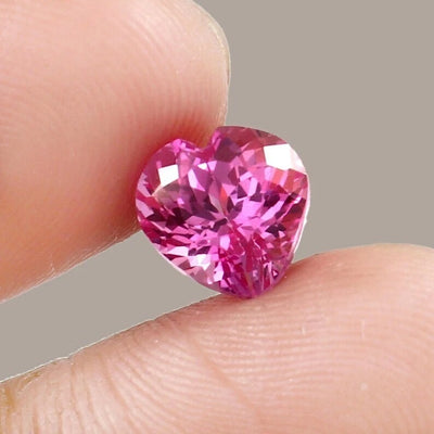 Heart-shaped pink sapphire gemstone held between fingers against a neutral background