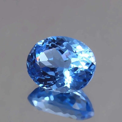 Blue Tourmaline Unheated gemstone on a reflective surface with a neutral background