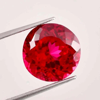 ruby Round red gemstone held by tweezers on a light gray background