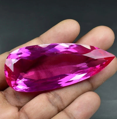 Hand holding a large Royal Pink Ceylon Sapphire gemstone against a dark background