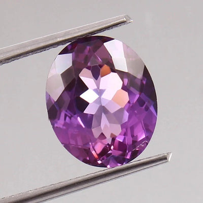 Taaffeite gemstone held between tweezers on a light gray background