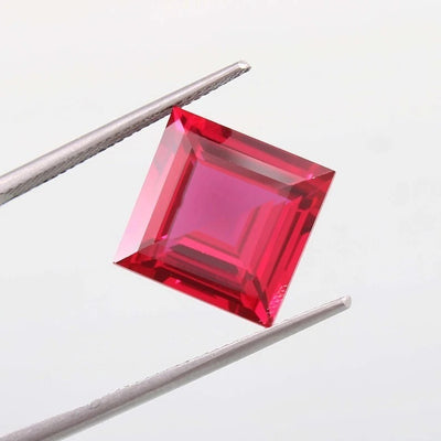 Square-cut red Mozambique Ruby gemstone held by tweezers against a light gray background