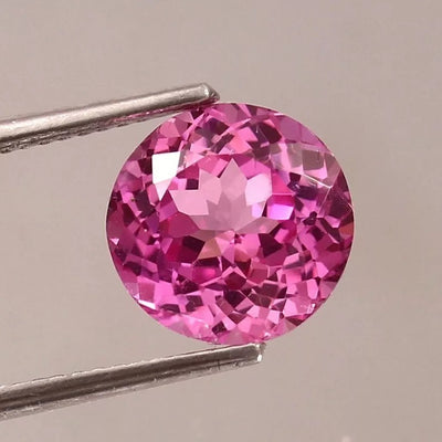 Ceylon Pink Sapphire gemstone held by tweezers against a neutral background