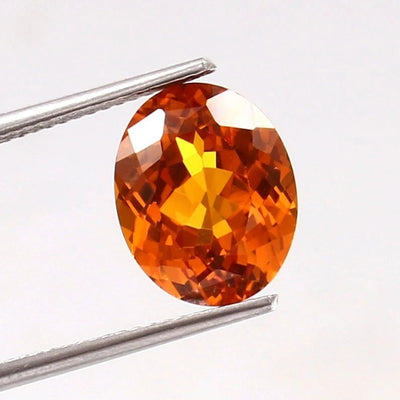 Ceylon Orange Sapphire gemstone held between tweezers on a white background
