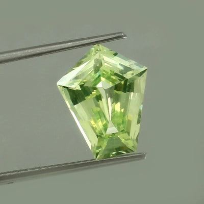 Green Chrysoberyl gemstone held by tweezers against a gray background