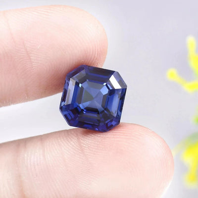 Blue Sapphire gemstone held between two fingers against a neutral background