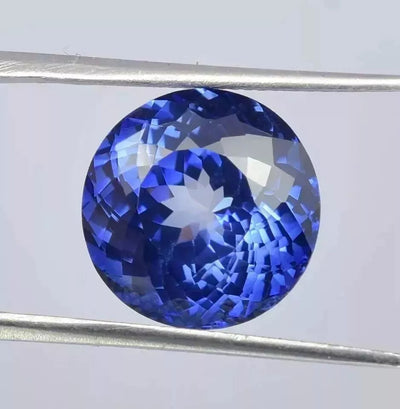 Royal Blue Sapphire gemstone held between two metal prongs on a light gray background