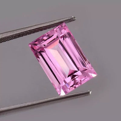 Pink Baguette Cut sapphire gemstone held by tweezers on a gray background