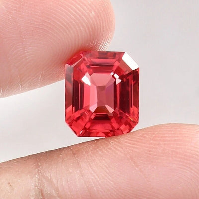 Padparadscha Sapphire gemstone held between two fingers against a neutral background
