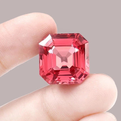 Padparadscha Sapphire gemstone held between fingers against a gray background
