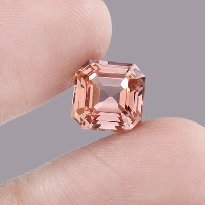 Padparadscha Sapphire – Peach gemstone held between fingers against a neutral background