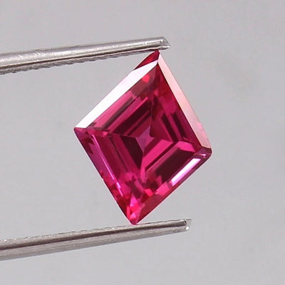 Lozenge Pink Sapphire 
gemstone held by tweezers against a gray background