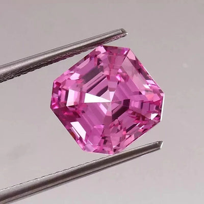 Ceylon Pink Sapphire gemstone held between tweezers on a gray background