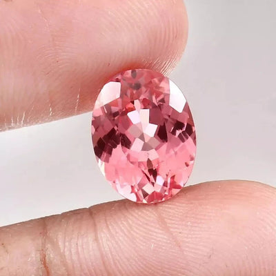 Padparadscha Sapphire Peach To Pink gemstone held between fingers against a neutral background