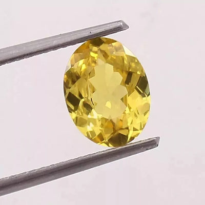 Yellow Sapphire gemstone held between tweezers against a light gray background