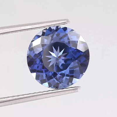 Royal Blue Sapphire Round Cut gemstone held by tweezers on a light gray background