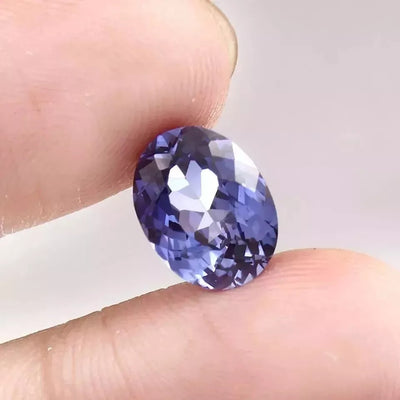 Blue Sapphire gemstone held between two fingers against a white background