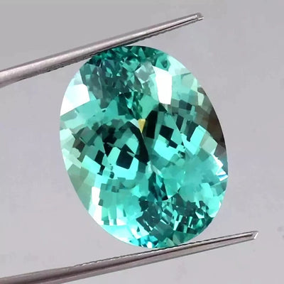 Bi-Color Parti-Sapphire gemstone held between tweezers on a gray background