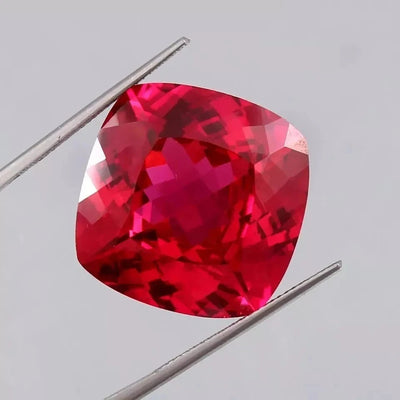 Blood Red Ruby gemstone held between tweezers on a light gray background