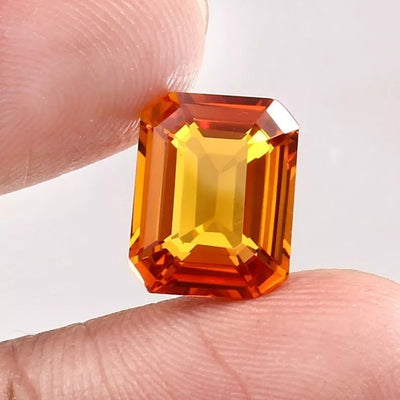 Orange Sapphire gemstone held between fingers against a white background