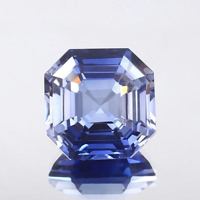 Faceted Cornflower Blue Sapphire gemstone on a light gray background