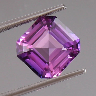 Hexagonal Purple Pink Sapphire gemstone held between tweezers on a gray background