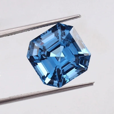 Swiss Blue Topaz gemstone held between tweezers on a light gray background