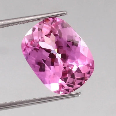 Unheated Sapphire gemstone held by tweezers on a gray background