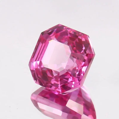 Faceted Natural Pink Sapphire gemstone on a reflective surface with a light gray background