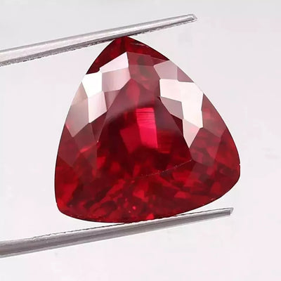 Mozambique Blood Red Ruby Trillion Cut gemstone held by tweezers on a white background