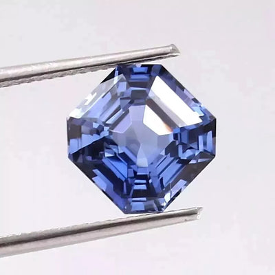 Royal Blue Sapphire gemstone held by tweezers against a white background