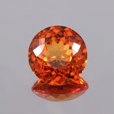 Faceted Orange Sapphire gemstone on a reflective gray surface