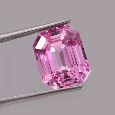 Pink Padparadscha Sapphire gemstone held by tweezers on a gray background