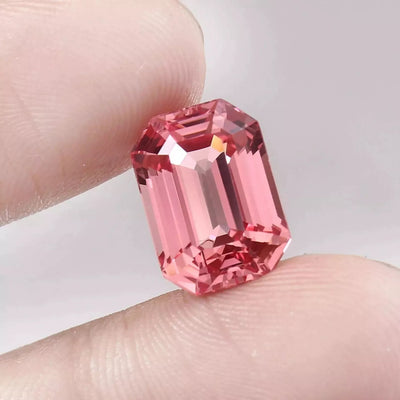 Padparadscha Sapphire Peach to Pink gemstone held between two fingers against a neutral background