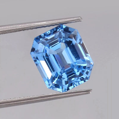 Blue sapphire gemstone held between tweezers on a gray background