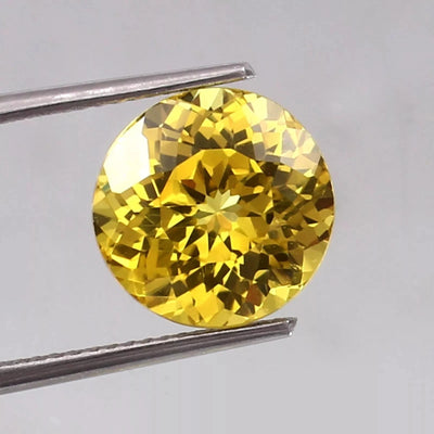 Ceylon Yellow Sapphire gemstone held between tweezers on a light gray background